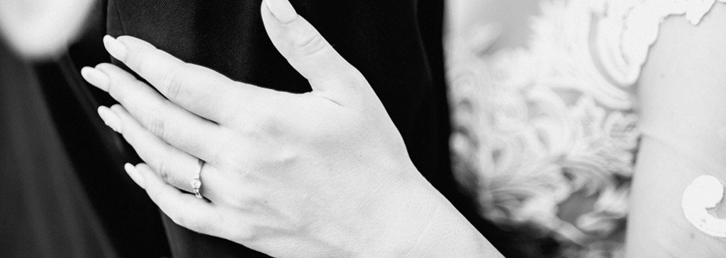 black and white photo of a newlywed couple, groom and bride holding hands with rings