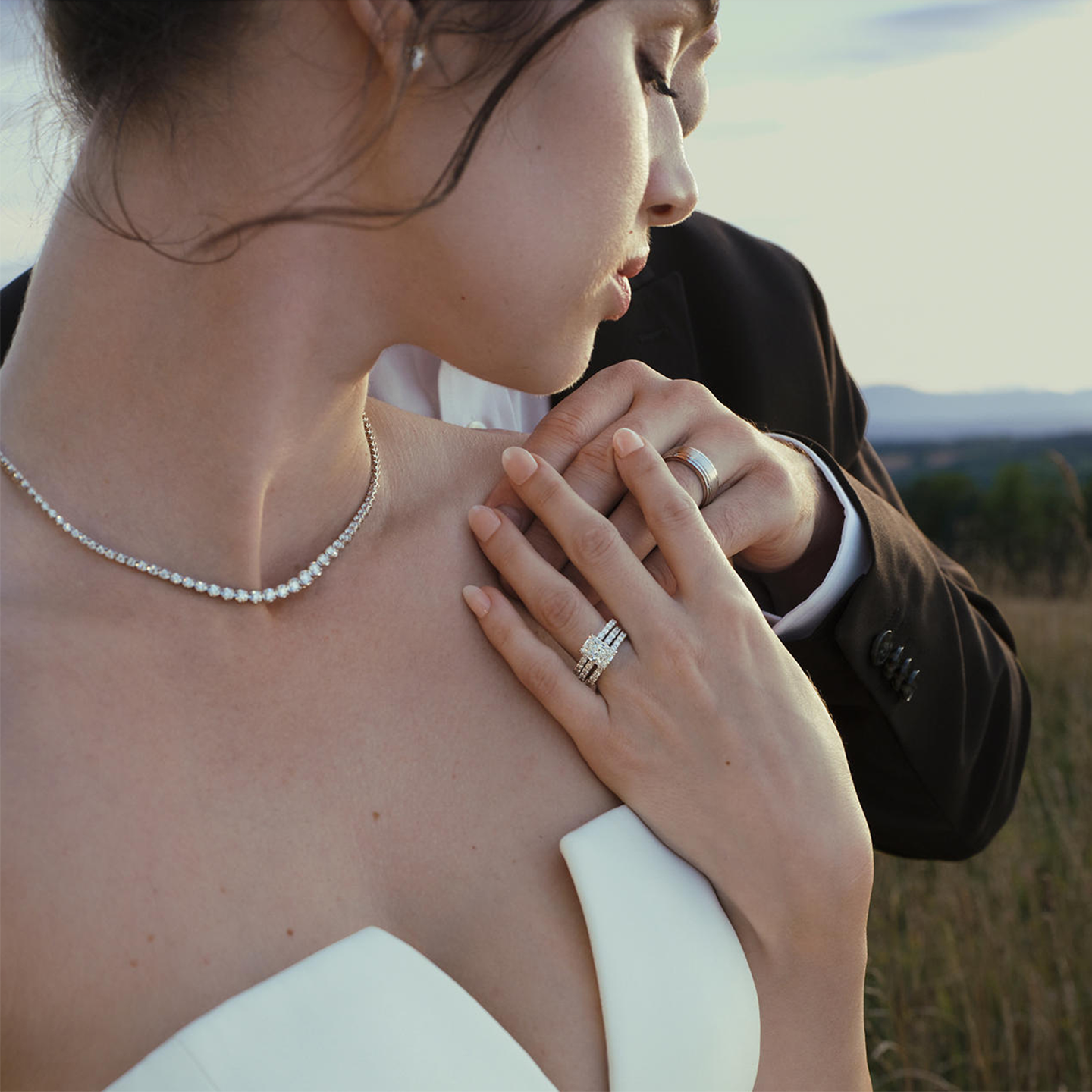 A bride and groom standing in a field showing off their wedding rings from the Vera Wang Love Collection.