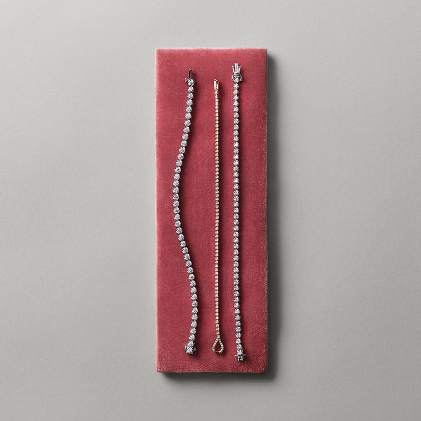 Three diamond tennis bracelets laid on top of a red cushion from the Zales Essentials Collection.