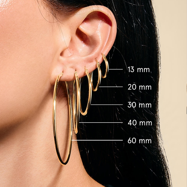 A model wearing five different sized gold, hoop earrings.