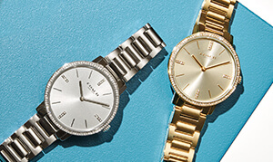 Two analog watches - one silver and one gold - on a blue background