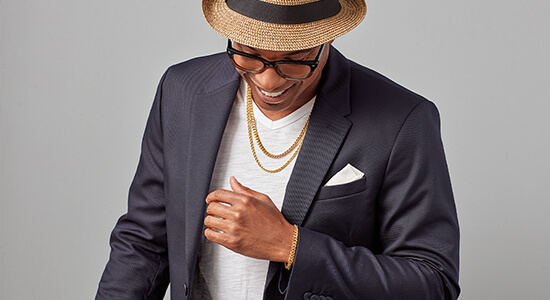 A man wearing a blue blazer, hat and two gold chains