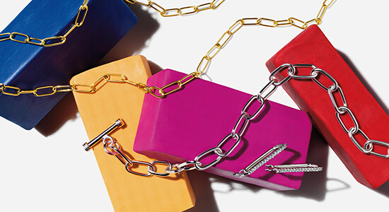 A gold chain, silver bracelet and silver earrings laid across multi-colored blocks