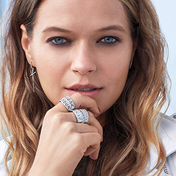 A woman holding her chin and showing off several wide diamond rings